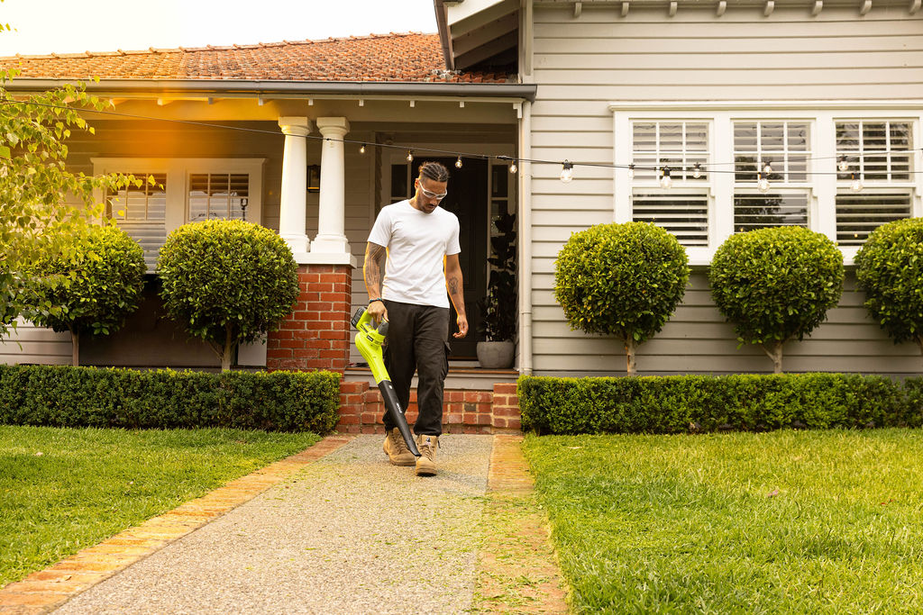 A man uses a RYOBI Leaf Blower to clear lawn trimmings off his footpath