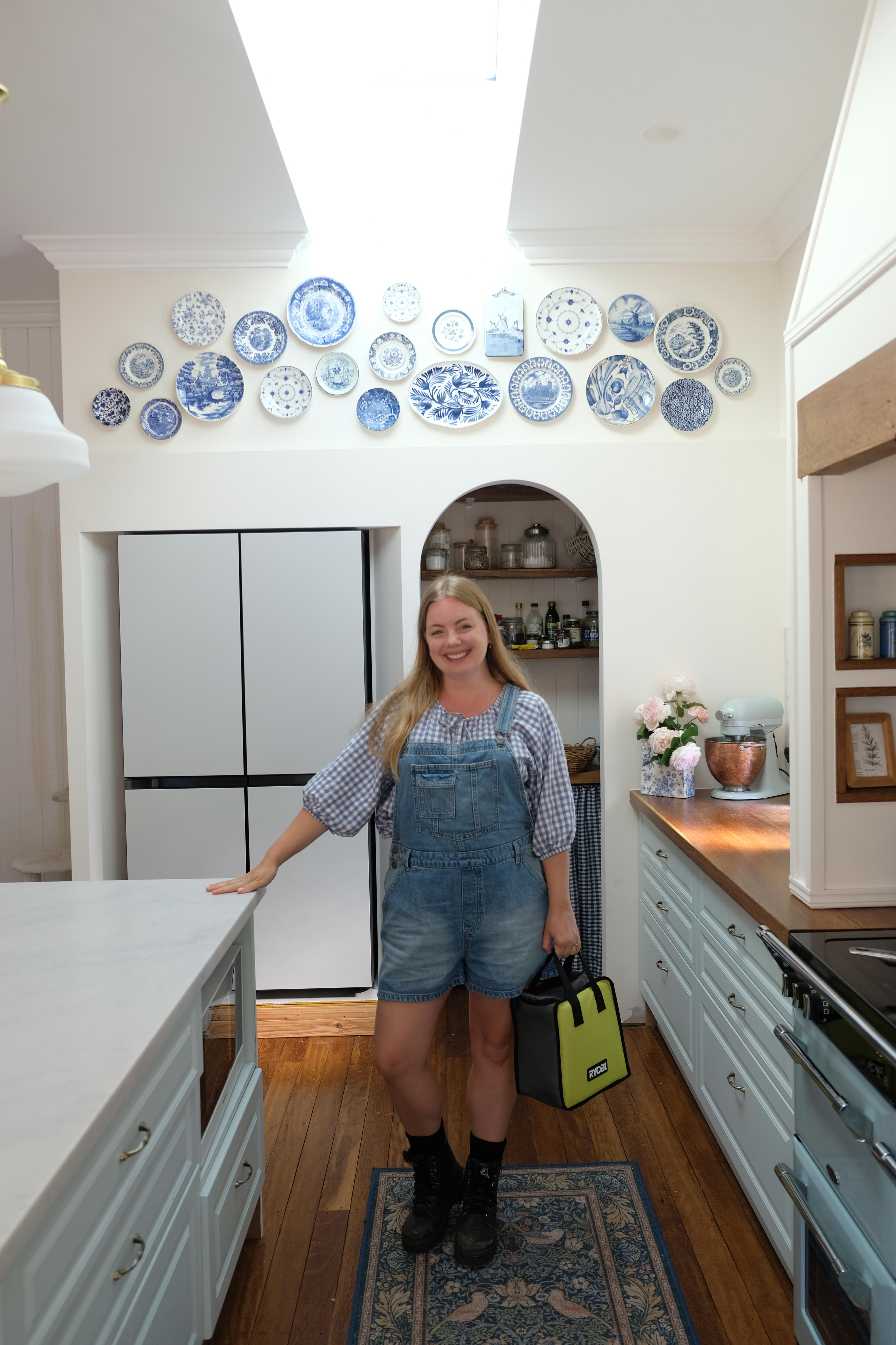 Brooke Styles poses in front of DIY Plate Gallery Wall. She is holding a RYOBI workbag and smiling. 