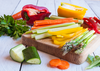 A wooden chopping board with sliced asparagus, capsicum, carrots, zucchini and more